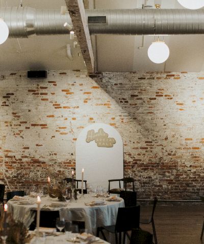 A stylish industrial-chic dining space with brick walls, round tables set for a meal, soft lighting, and a decorative arched doorway, cozy vibes.