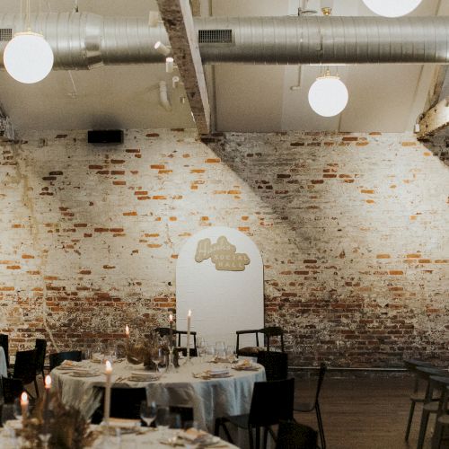 A stylish industrial-chic dining space with brick walls, round tables set for a meal, soft lighting, and a decorative arched doorway, cozy vibes.