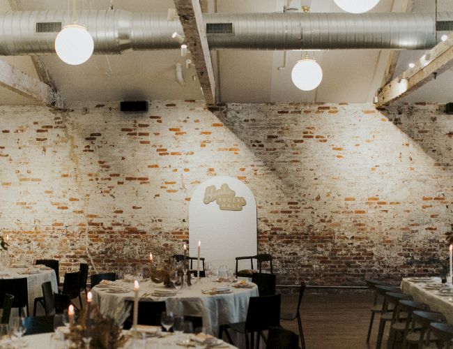 A stylish industrial-chic dining space with brick walls, round tables set for a meal, soft lighting, and a decorative arched doorway, cozy vibes.