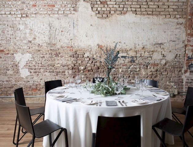 A formal dining setup: a long table with a white tablecloth, place settings, candles, and floral centerpieces, in a dimly lit, elegant room.