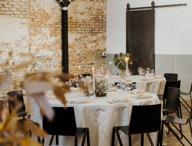 A modern cafe or restaurant with wooden chairs, tables, warm lighting, and a person in the background. Top it at 140 characters, always ending the sentence.