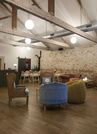 A bright, airy lounge with exposed brick walls, wooden beams, and round pendant lights, featuring colorful armchairs and a mix of seating areas.