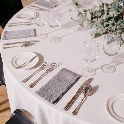 Silverware, glassware, and a white tablecloth set for a formal meal; a green centerpiece and neatly folded napkins atop the table.