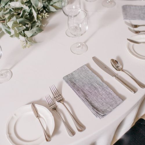 A formal banquet table setup with white linens, glassware, silverware, a napkin, and a floral centerpiece.