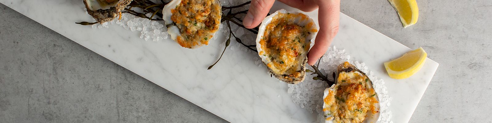 A person&rsquo;s hand places baked stuffed mushrooms on a tray, with salt crystals and fresh lemon slices around them.