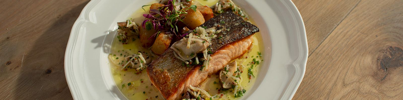 A plated seared salmon fillet with herb garnish and vegetables in a creamy sauce, served on a white dish.