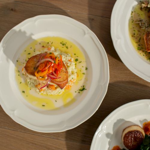 Two gourmet plates of fish and seafood in creamy yellow sauce, garnished with herbs, onions, and vegetables.