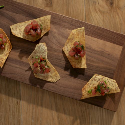 Crispy tostada chips topped with diced tomato, herbs, and green onion on a wooden board.