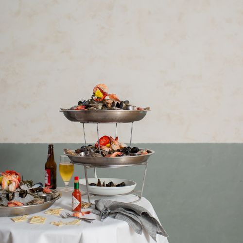 A seafood buffet on a table: mussels and shrimp in stacked chafing dishes, with sauces and glasses nearby.