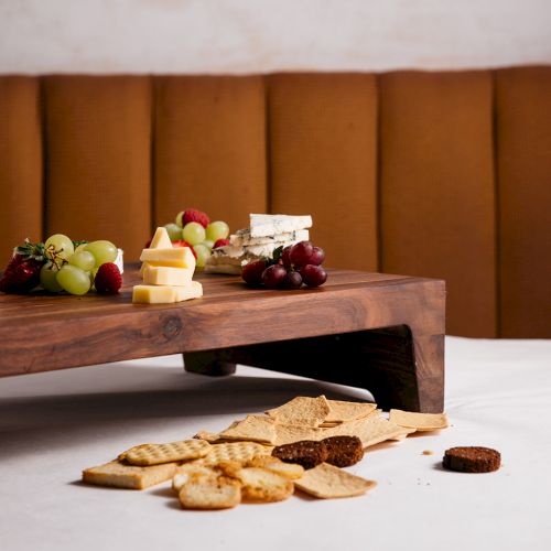 A rustic cheese board with cheddar and brie, topped with grapes, strawberries, and served alongside crackers on a wooden table, enjoy!